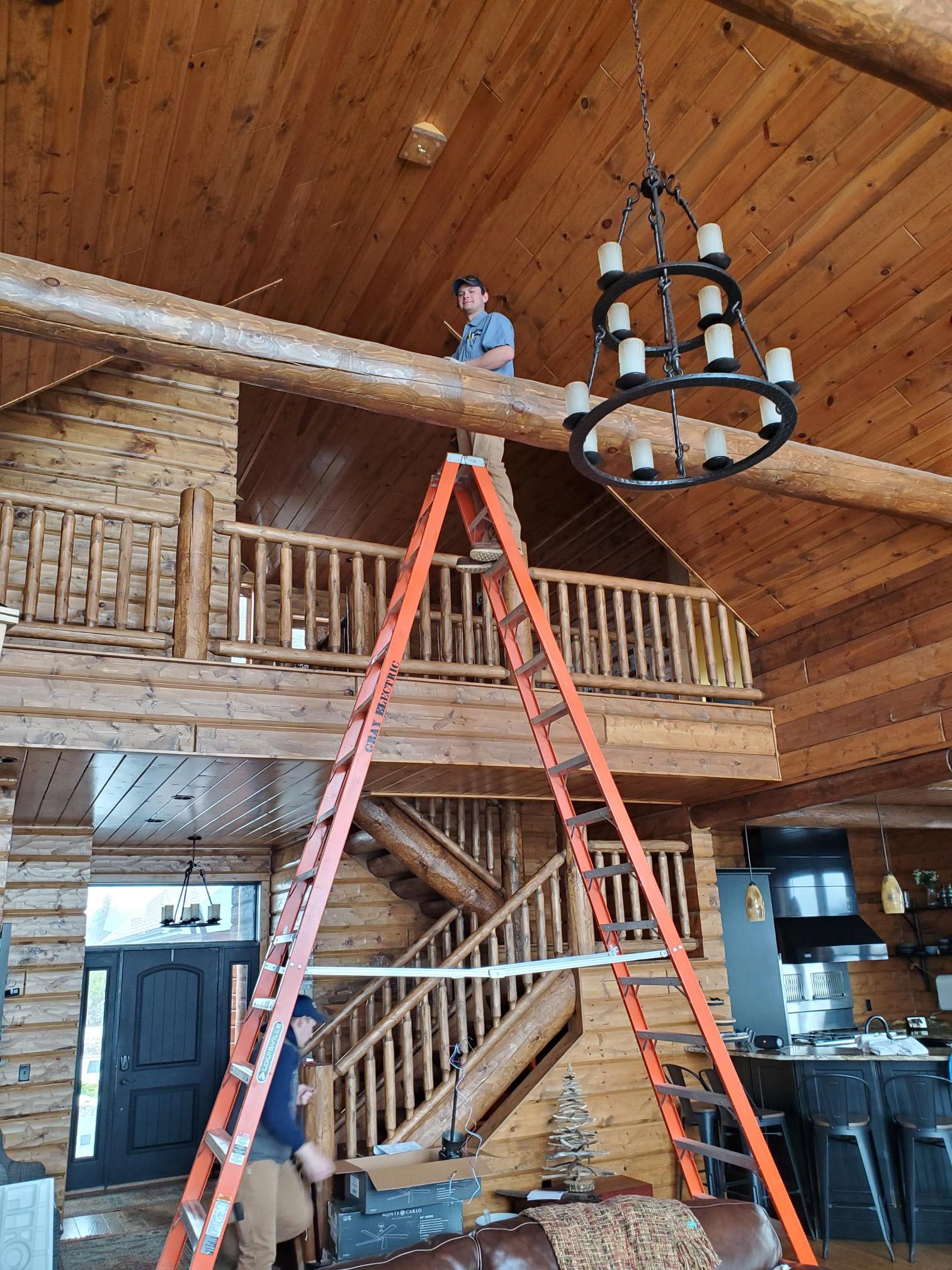 A Gray Electric electrician installing a light fixture in a log home